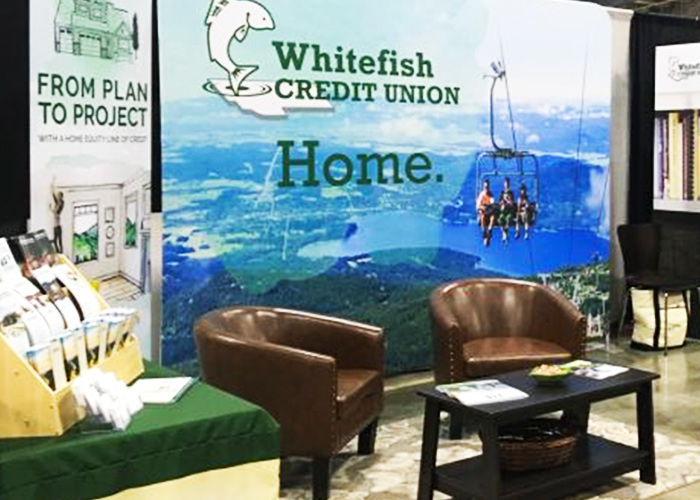 Tradeshow booth event photo showing brochures, cozy seating, and Summer chairlift backdrop